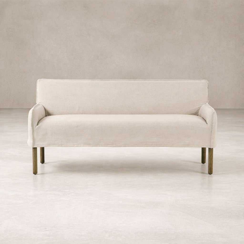 Slipcovered upholstered bench in cream fabric with a low back and wood legs.