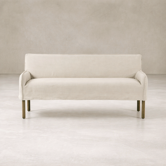 Slipcovered upholstered bench in cream fabric with a low back and wood legs.