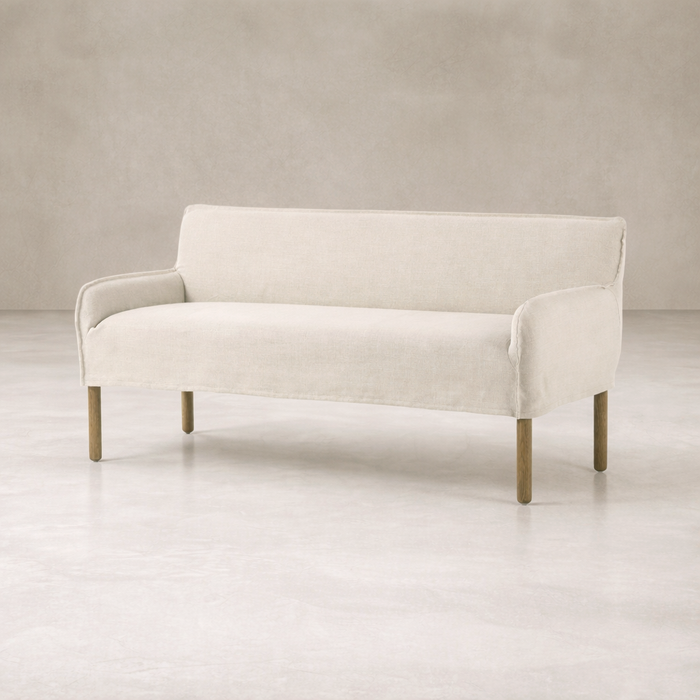 Slipcovered upholstered bench in cream fabric with a low back and wood legs.