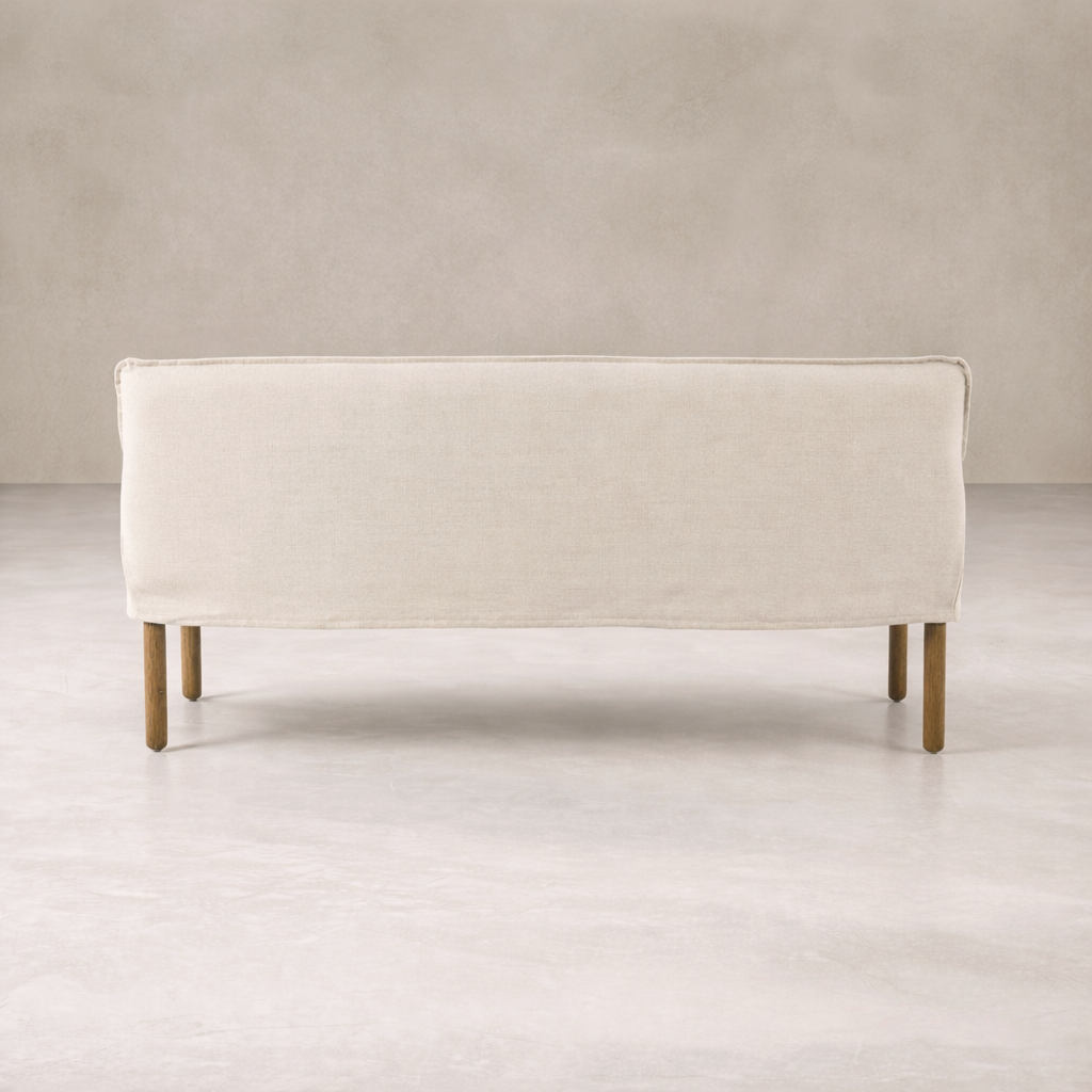 Slipcovered upholstered bench in cream fabric with a low back and wood legs.