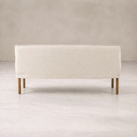 Slipcovered upholstered bench in cream fabric with a low back and wood legs.