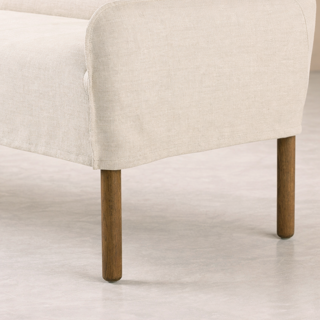 Slipcovered upholstered bench in cream fabric with a low back and wood legs.