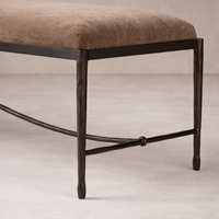 Long upholstered bench with a warm brown cushion and hand-forged iron base