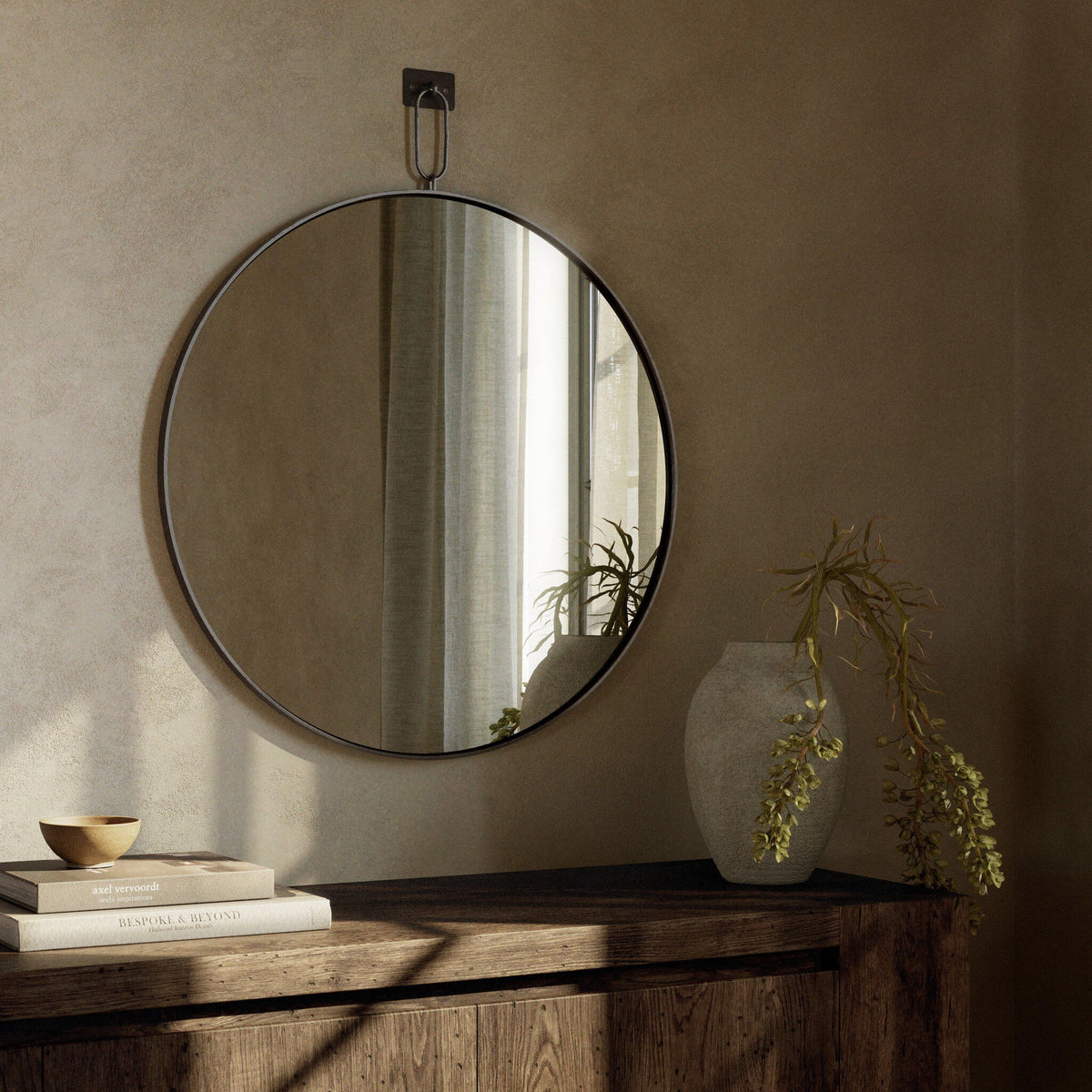 Round Vida Mirror with a sleek metal frame, reflecting natural light in a cozy room.