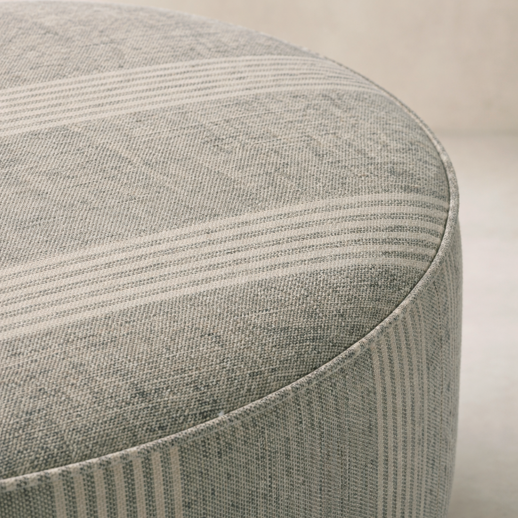 Close-up of the Bilbury Large Round Ottoman featuring a textured fabric in soft gray tones.